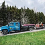 A truck with a trailer transporting a large piece of wood down a road.