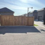 A driveway featuring a wooden fence alongside a parked truck under clear skies.