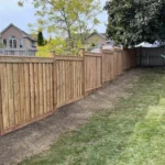 A wooden fence encloses a backyard featuring a well-maintained green lawn.