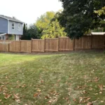 A backyard featuring a wooden fence surrounding a well-maintained green lawn.