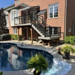 A swimming pool with a deck and stairs leading up to a house in the background.